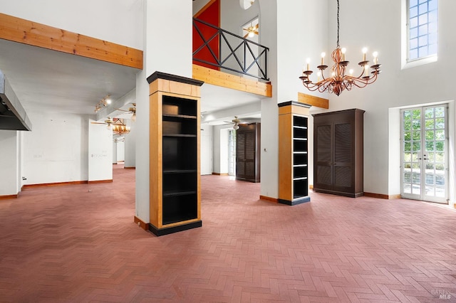 unfurnished living room with ceiling fan with notable chandelier, baseboards, and a towering ceiling