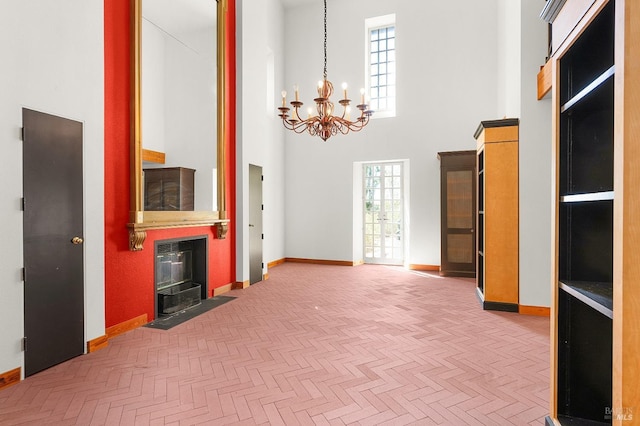 interior space featuring baseboards, a notable chandelier, a towering ceiling, and a fireplace with flush hearth