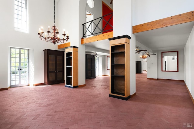 unfurnished living room with baseboards, arched walkways, a towering ceiling, and ceiling fan with notable chandelier