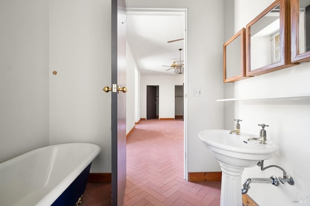 bathroom featuring ceiling fan, a freestanding bath, brick floor, and baseboards