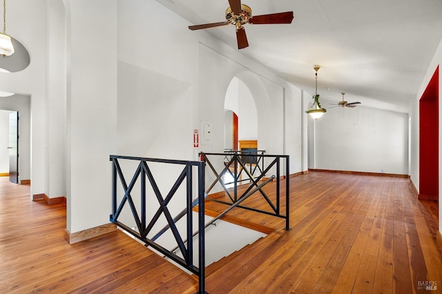 corridor with an upstairs landing, high vaulted ceiling, hardwood / wood-style flooring, arched walkways, and baseboards