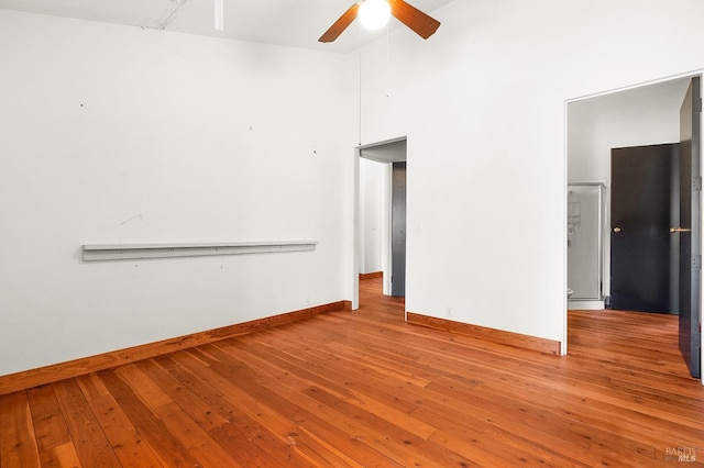 empty room with baseboards, a high ceiling, ceiling fan, and hardwood / wood-style flooring