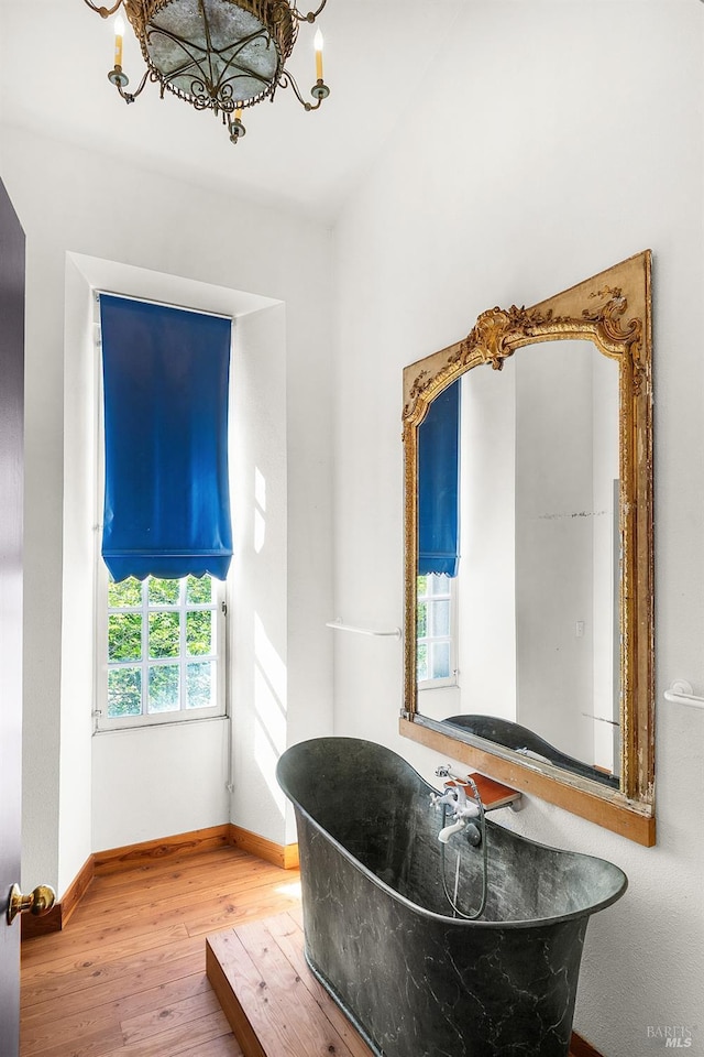 bathroom featuring hardwood / wood-style floors, a notable chandelier, baseboards, and a freestanding bath