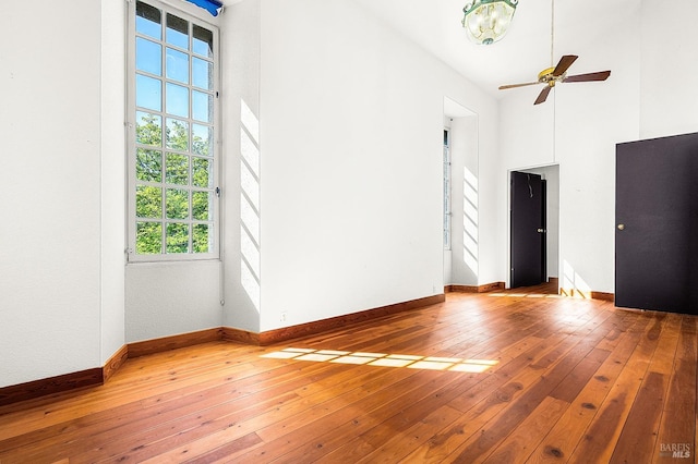 spare room featuring baseboards, wood-type flooring, and a high ceiling