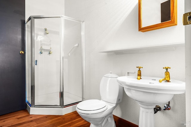 bathroom with a stall shower, toilet, and wood finished floors