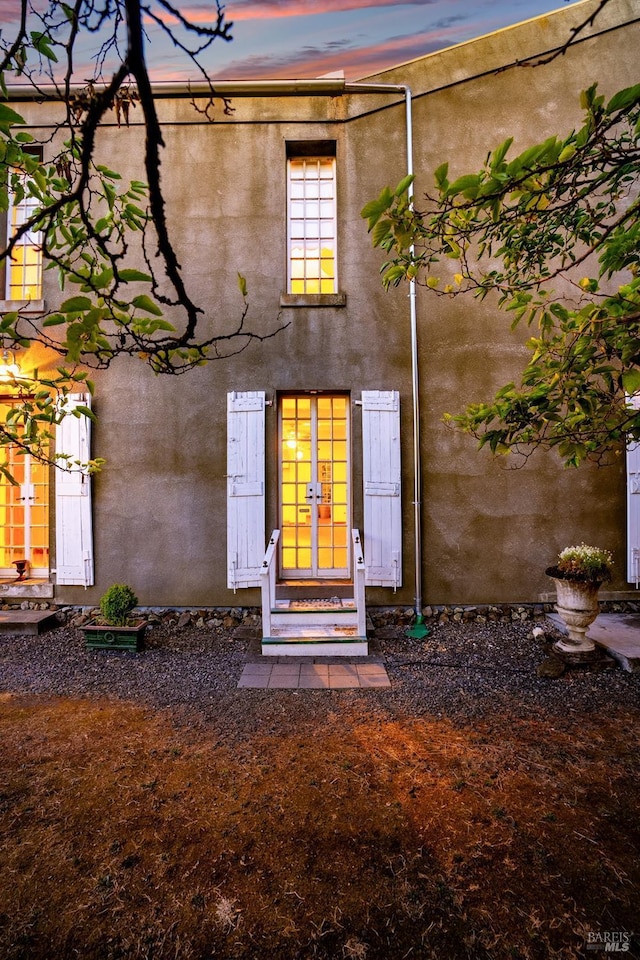 back of property at dusk with french doors and stucco siding