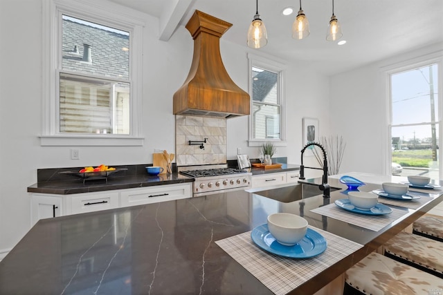 kitchen featuring stove, custom range hood, sink, pendant lighting, and white cabinetry