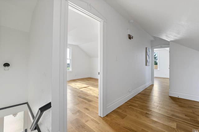 hallway featuring light hardwood / wood-style flooring, vaulted ceiling, and plenty of natural light