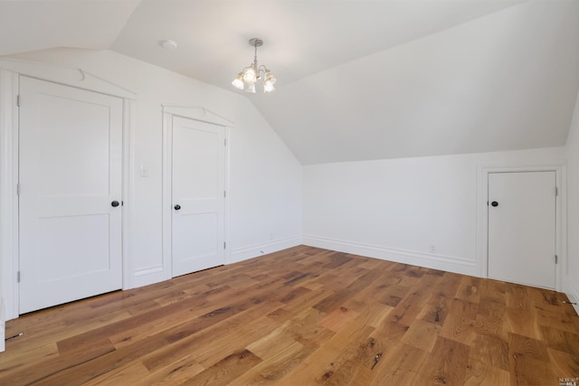 bonus room with wood-type flooring, vaulted ceiling, and a notable chandelier