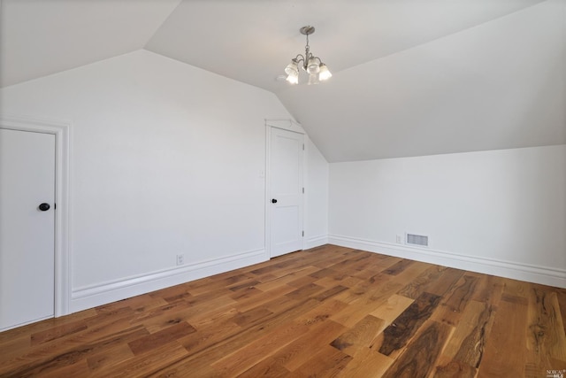 additional living space with hardwood / wood-style flooring, an inviting chandelier, and lofted ceiling