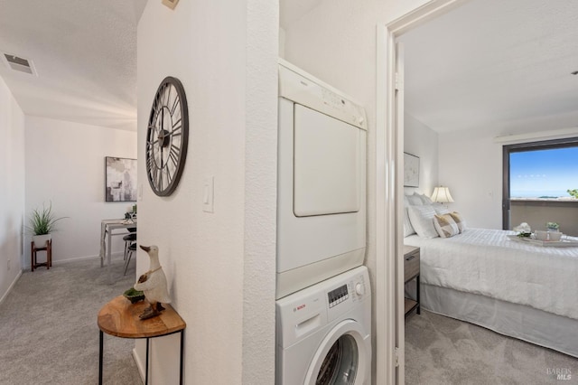 clothes washing area featuring a textured ceiling, light carpet, and stacked washing maching and dryer