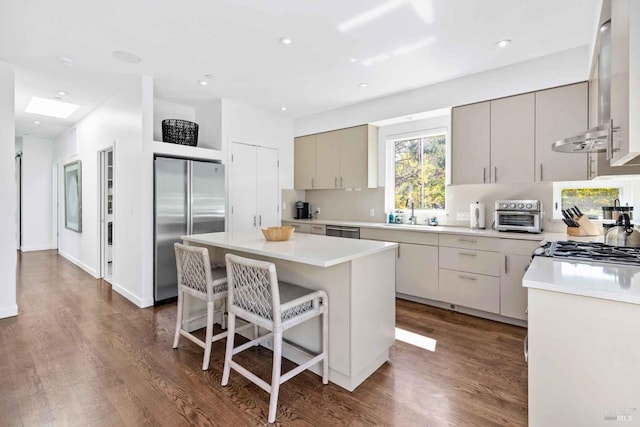 kitchen featuring dark wood-type flooring, wall chimney exhaust hood, a kitchen bar, a center island, and stainless steel appliances