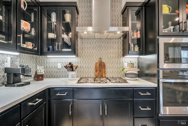 kitchen featuring backsplash, light stone counters, stainless steel appliances, and wall chimney range hood