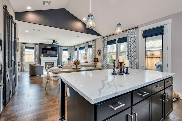 kitchen with light stone countertops, a center island, dark hardwood / wood-style flooring, lofted ceiling, and decorative light fixtures