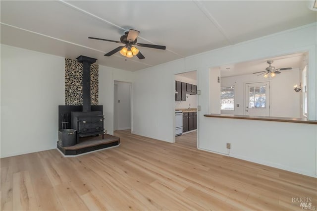 unfurnished living room featuring ceiling fan, a wood stove, and light hardwood / wood-style flooring