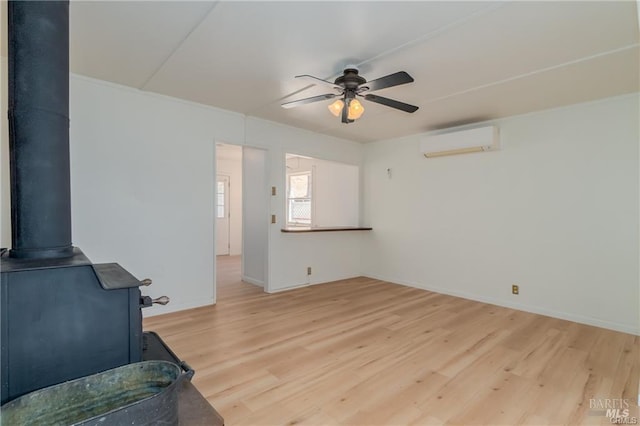 living room with a wall mounted AC, ceiling fan, a wood stove, and light hardwood / wood-style flooring