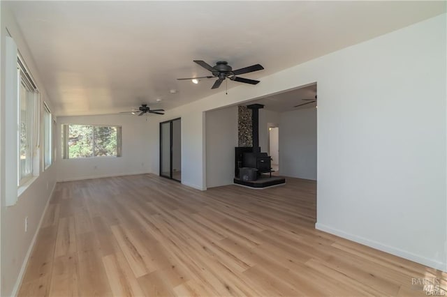 unfurnished living room with lofted ceiling, light hardwood / wood-style flooring, ceiling fan, and a wood stove