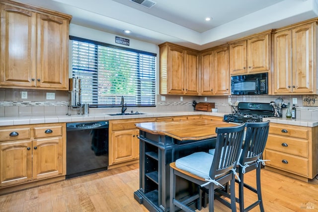 kitchen featuring tasteful backsplash, sink, black appliances, tile countertops, and light hardwood / wood-style flooring