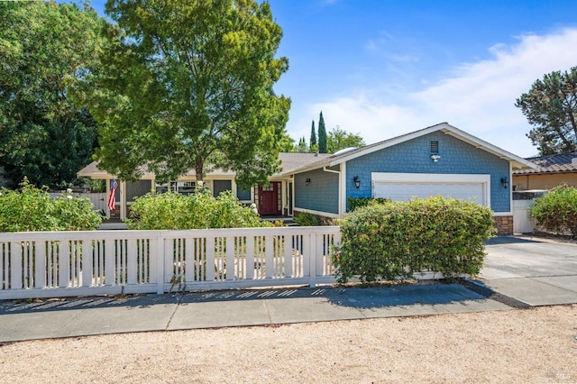 view of front of home with driveway, stone siding, a garage, and a fenced front yard