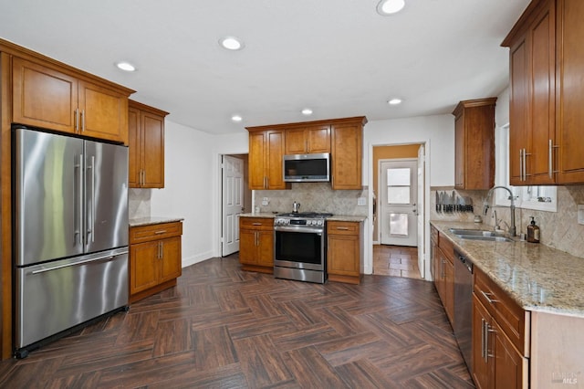 kitchen featuring a sink, light stone counters, recessed lighting, stainless steel appliances, and brown cabinetry