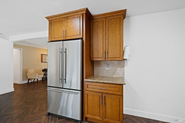 kitchen with light stone counters, tasteful backsplash, brown cabinetry, baseboards, and high end refrigerator