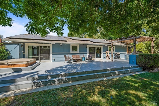 back of property with a deck, a covered hot tub, a pergola, and solar panels