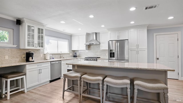 kitchen featuring wall chimney range hood, a kitchen breakfast bar, white cabinets, and appliances with stainless steel finishes