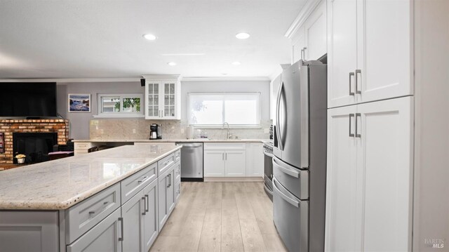 kitchen featuring white cabinetry, ornamental molding, stainless steel appliances, light stone countertops, and a brick fireplace