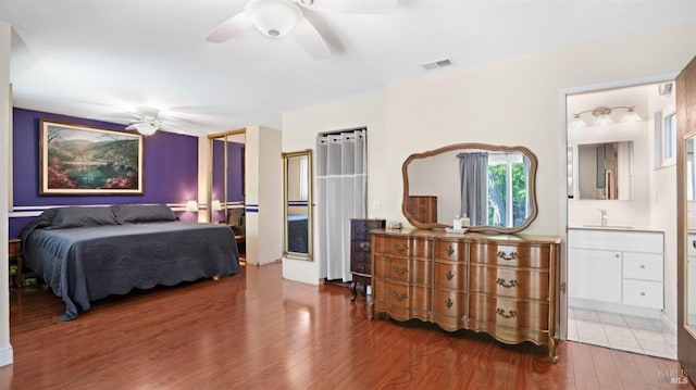 bedroom with visible vents, connected bathroom, ceiling fan, wood finished floors, and a sink