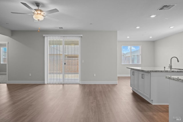 unfurnished living room with visible vents, ceiling fan, a sink, and wood finished floors