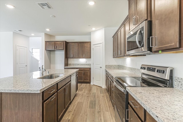 kitchen featuring light stone counters, an island with sink, light wood-type flooring, appliances with stainless steel finishes, and sink