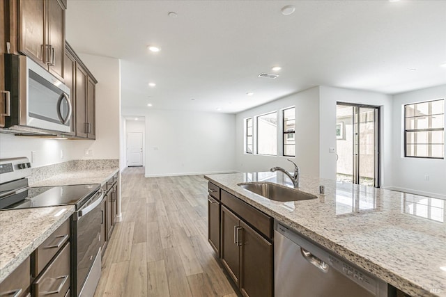 kitchen featuring stainless steel appliances, light stone countertops, light hardwood / wood-style flooring, and sink