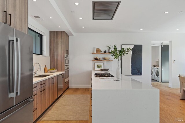 kitchen featuring light wood-style flooring, a sink, appliances with stainless steel finishes, modern cabinets, and washing machine and clothes dryer