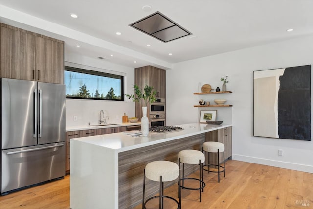 kitchen featuring modern cabinets, appliances with stainless steel finishes, a breakfast bar area, open shelves, and a sink