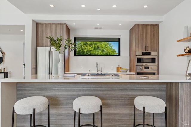 kitchen with brown cabinets, stainless steel appliances, light countertops, visible vents, and modern cabinets