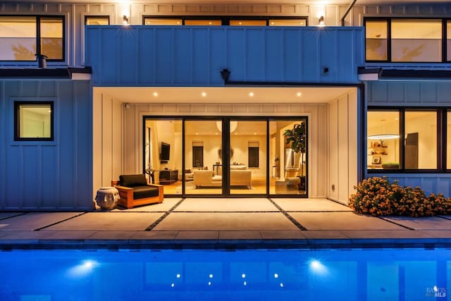 rear view of property featuring a patio area, an outdoor pool, and board and batten siding