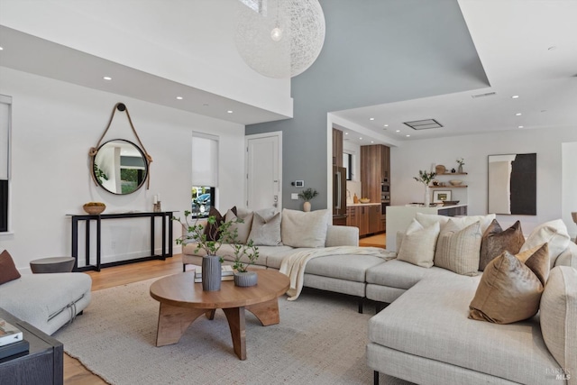 living room with a high ceiling, recessed lighting, visible vents, and light wood-style floors