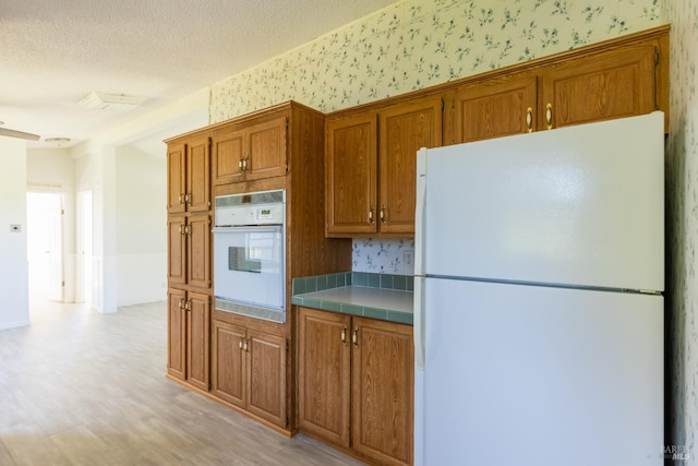 kitchen with tile countertops, white appliances, a textured ceiling, and light hardwood / wood-style flooring