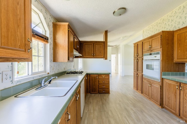 kitchen featuring oven, light wood-type flooring, a textured ceiling, and sink