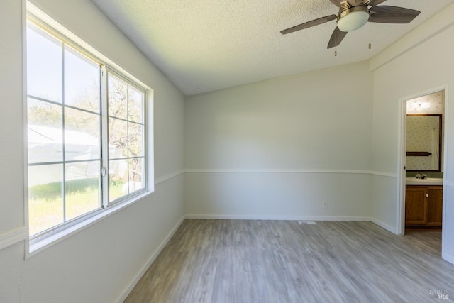 empty room with light wood-type flooring, lofted ceiling, ceiling fan, and a textured ceiling