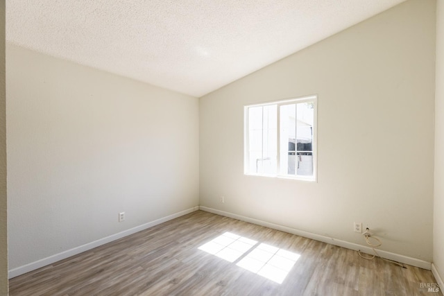 empty room with lofted ceiling, wood-type flooring, and a textured ceiling