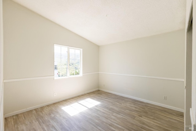 empty room with a textured ceiling, lofted ceiling, and light hardwood / wood-style floors