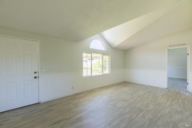 spare room featuring a textured ceiling, vaulted ceiling, and hardwood / wood-style flooring