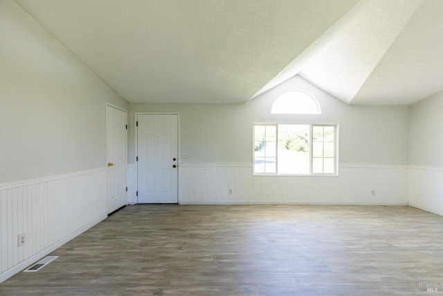 empty room with light wood-type flooring, lofted ceiling, and a textured ceiling