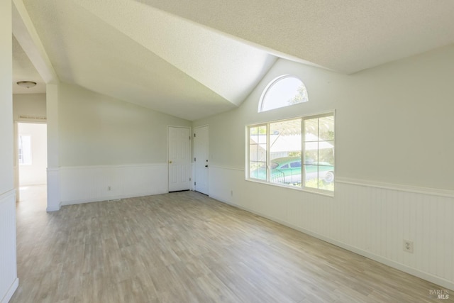 additional living space featuring a textured ceiling, vaulted ceiling, and light wood-type flooring