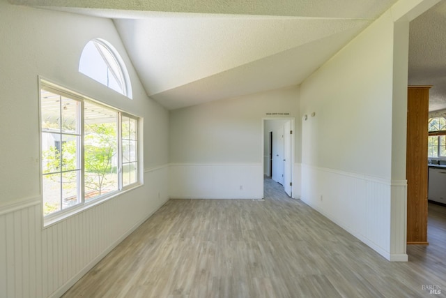 unfurnished room featuring a textured ceiling, vaulted ceiling, and light hardwood / wood-style floors