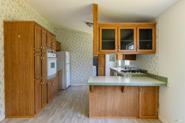 kitchen featuring white appliances, light hardwood / wood-style flooring, a kitchen bar, a textured ceiling, and kitchen peninsula