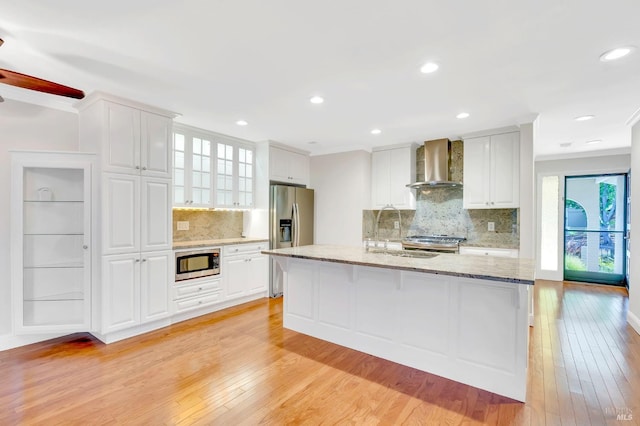 kitchen with appliances with stainless steel finishes, white cabinets, wall chimney range hood, and light wood-type flooring