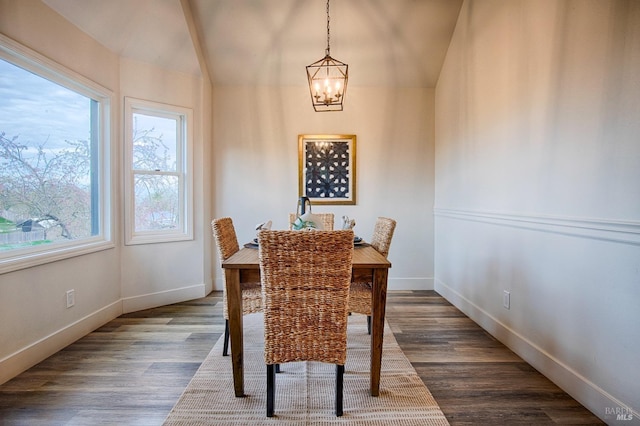 dining space featuring dark wood-style floors, lofted ceiling, a chandelier, and baseboards