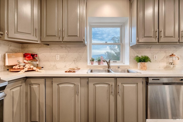 kitchen featuring tasteful backsplash, light countertops, gray cabinetry, stainless steel dishwasher, and a sink